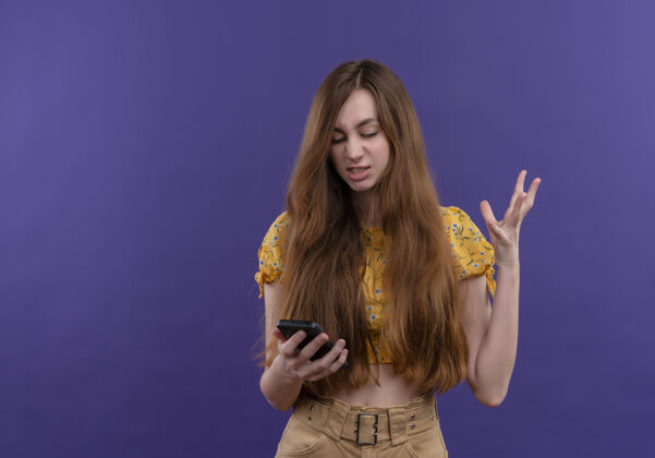 复制恼怒的年轻女孩拿着手机 举起手在孤立的紫色空间与复制空间电话手持有
