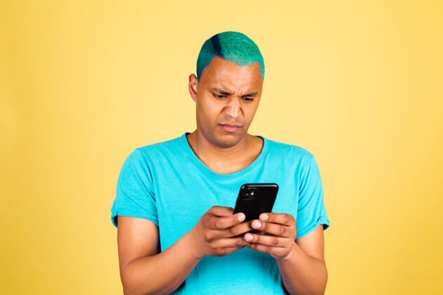 累非洲黑人男子在随意的黄色墙壁上用手机表情厌恶 满脸不满的负面情绪表情问题社交媒体