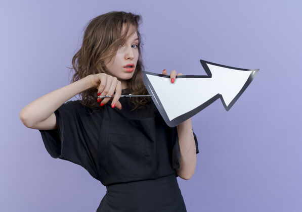 标记自信的年轻斯拉夫女理发师穿着制服 手里拿着剪刀和箭标 这是指在一边试图切断箭标孤立的紫色背景剪试试年轻