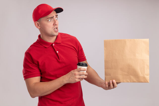 市民害怕地看着身边穿着制服戴着帽子的年轻送货员拿着纸食品包 把一杯咖啡隔在白色的墙上咖啡拿着制服