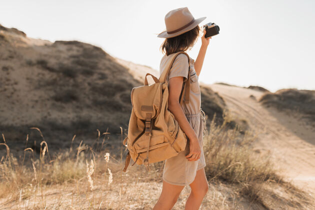 休闲穿着卡其色衣服的时髦年轻女子在沙漠中行走 在非洲旅行 戴着帽子和背包 用老式相机拍照夏天人狩猎