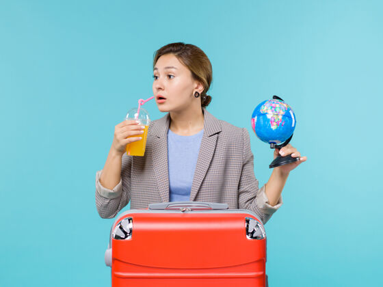 肖像前景度假中的女性手持鲜果汁和浅蓝色书桌上的地球仪出海度假风景航行旅行