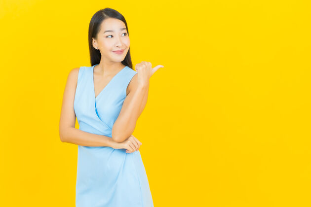 人在黄色墙壁上描绘美丽的亚洲年轻女子微笑的动作欢呼时尚漂亮