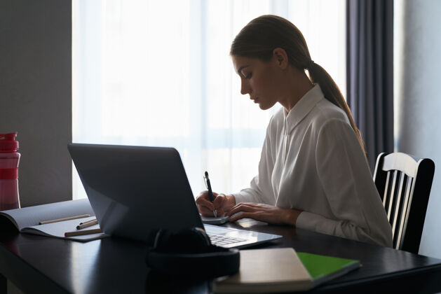 桌子专注的女人坐在桌边 用笔记本电脑工作距离远程肖像