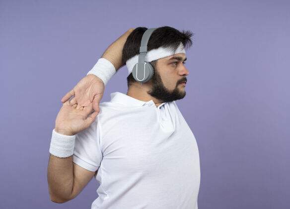 头带站在侧视图中的年轻运动型男子戴着头带和腕带 戴着耳机伸出手臂运动人物查看
