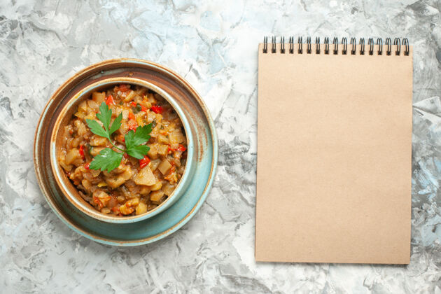晚餐碗里烤茄子沙拉的顶视图灰色表面上的笔记本食物餐碗