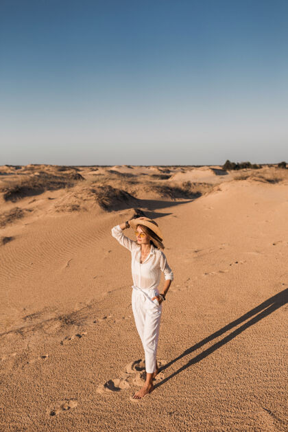 帽子一个穿着白色衣服 戴着草帽 在沙漠沙滩上行走的时尚美女人模特旅行者