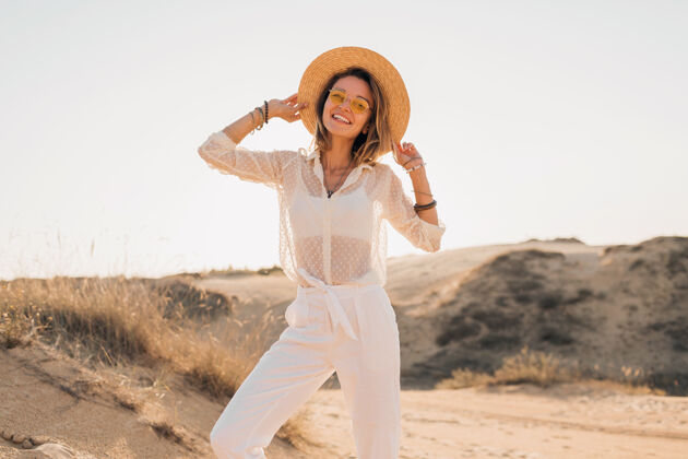 沙丘落日时分 阳光明媚的夏日 穿着白色衣服 戴着草帽和太阳镜 在沙漠的沙滩上摆出一副时髦 快乐 迷人的笑脸人女性度假