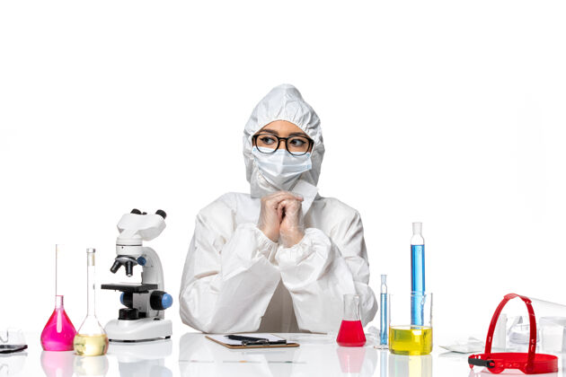诊所前视图穿着特殊防护服的女化学家坐在白色化学背景的溶液中-病毒大流行实验室外套医生视图