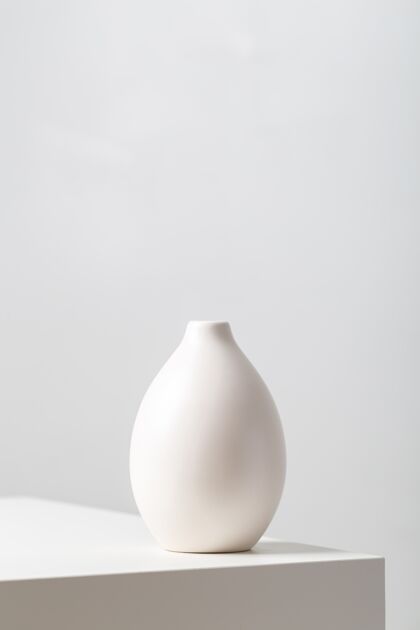 灯垂直特写一个白色的粘土花瓶在桌子上的灯光下映衬着一个白色的陶瓷空白容器