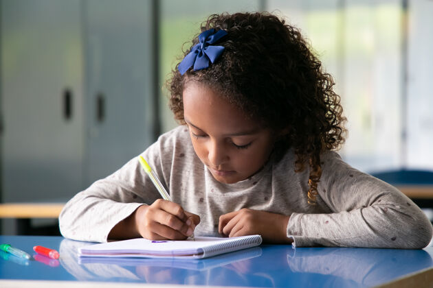 学校专注的混血女孩坐在学校的办公桌上 在抄写本上画画桌子童年女孩