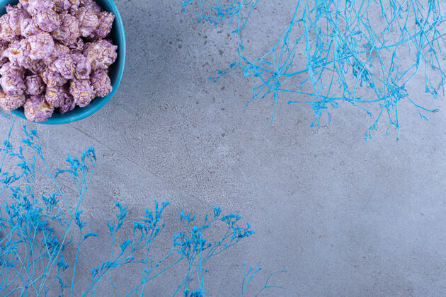 糖果蓝色的爆米花糖碗旁边是大理石表面的蓝色装饰树枝树枝碗玉米