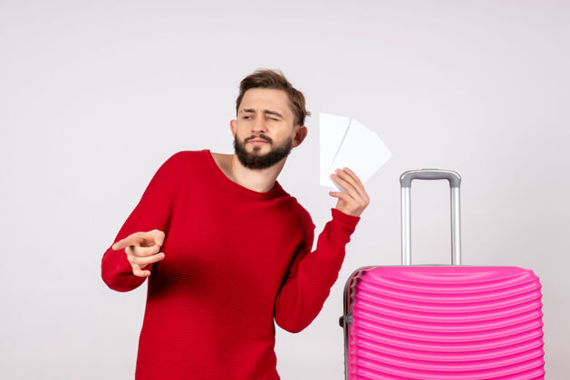 微笑正面图：年轻男性 带着粉色包 手持白墙彩色旅行机票 旅游度假男人度假航班