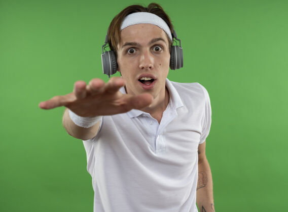 年轻人快乐的年轻人戴着头带 戴着护腕和耳机 手被隔离在绿色的墙上运动型耳机手握