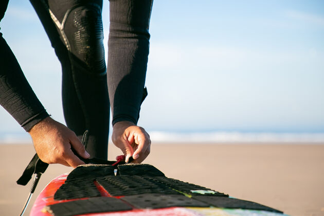 水在海边 穿着潜水服的冲浪者用手把冲浪板绑在脚踝上透明特写人