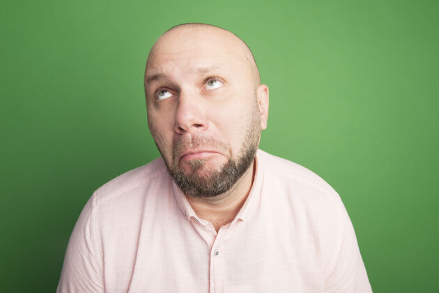 男人愁眉苦脸的中年秃头男人穿着粉色t恤隔离在绿色穿粉色秃顶