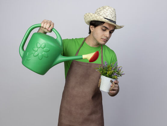 年轻自信的年轻男园丁穿着制服戴着园艺帽在花盆里用水壶浇花人男人制服
