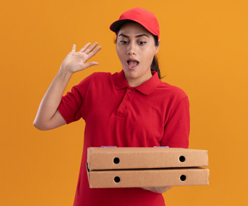 制服惊讶的年轻送货女孩穿着制服 戴着帽子 拿着披萨盒 举起手孤立在橙色的墙上送货披萨提高