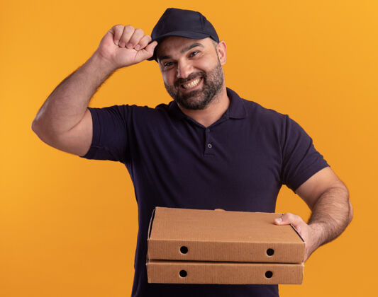 中年微笑的中年送货员穿着制服 戴着帽子 手里拿着披萨盒 手里拿着帽子 隔离在黄色的墙上制服送货微笑