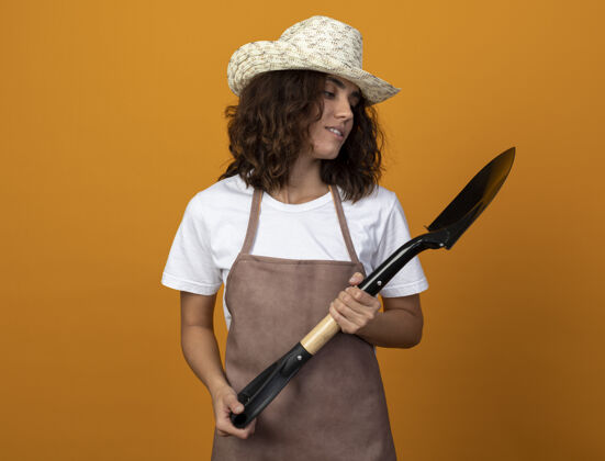 黑桃穿着制服的年轻女园丁戴着园艺帽 拿着铲子 看着铲子穿印象女人