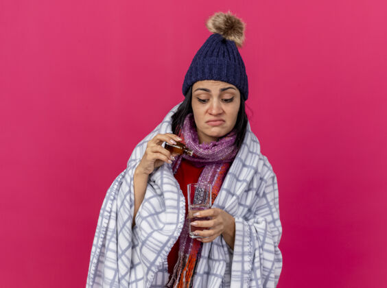 围巾专注的年轻病妇戴着冬天的帽子 围巾裹着格子布 往一杯水里加药 隔离在粉红色的墙上 留着复印空间集中穿着姿势