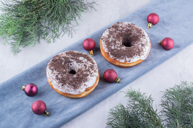烘焙两个甜甜圈和圣诞装饰品放在白色的折叠桌布上可口上釉圣诞