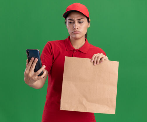 制服想着那个穿着制服 戴着帽子 拿着纸制食品包的年轻送货女孩 看着她手上的电话孤零零地贴在绿色的墙上帽子送货食物