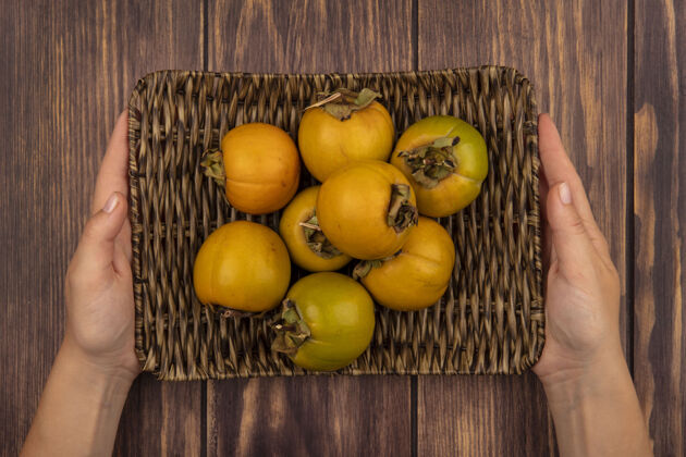 桔子俯视图：女性手拿柳条托盘的新鲜柿子水果放在木桌上柿子托盘木头