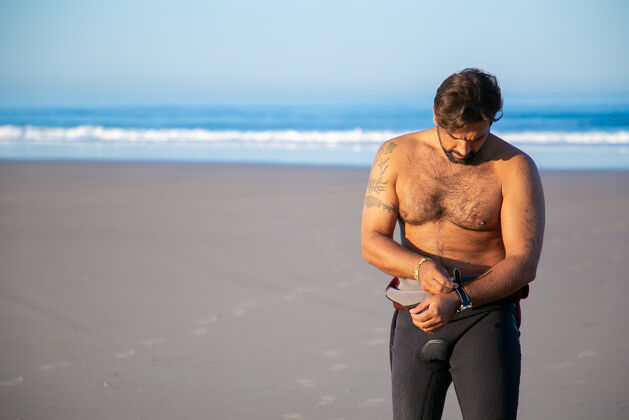 站立运动员穿上潜水衣在海边冲浪 然后脱下手表手表穿上男人
