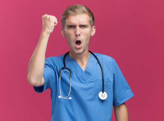 医生兴奋的年轻男医生穿着医生制服 听诊器显示“是”的手势 隔离在粉红色的墙上 留有复印空间手势展示兴奋