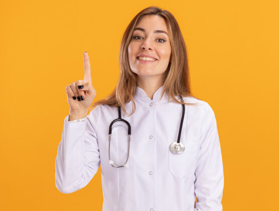 听诊器印象深刻的年轻女医生穿着医用长袍 用听诊器指着隔离在黄色墙上的那堵墙印象长袍年轻