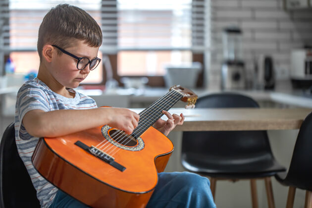 弦乐专注的小男孩坐在厨房里 手里拿着吉他小房间播放器