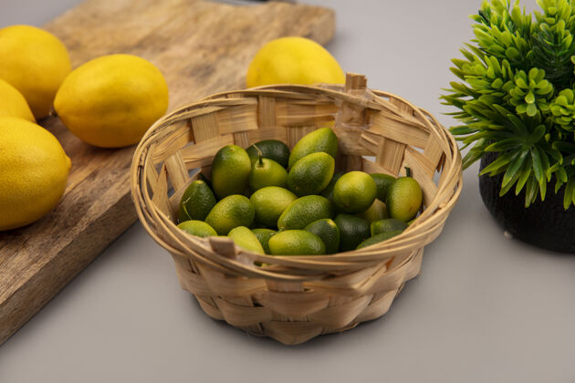桶绿色皮肤的金盏花在桶上的顶视图 灰色背景的木制厨房板上放着柠檬柠檬金盏花风景