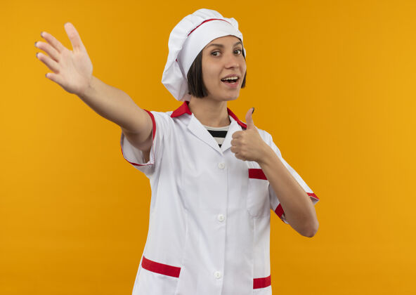 拇指身着厨师制服的快乐年轻女厨师向上竖起大拇指 在橘子色的地板上伸出手来厨师女性烹饪