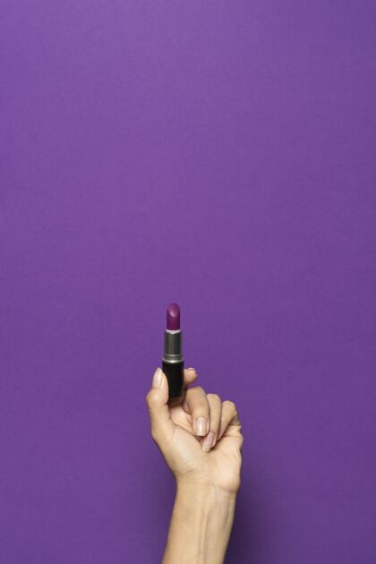 配件竖立的手拿着一个在紫色背景上隔离的口红化妆垂直美容