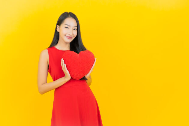 华丽在黄色的墙上画着美丽的亚洲年轻女子微笑的心枕形状一红色人