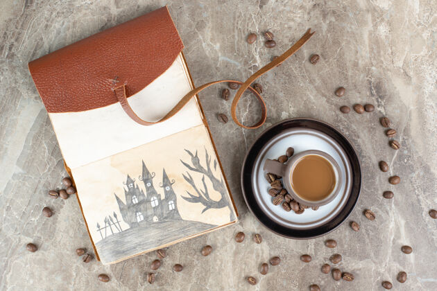 香味咖啡杯 咖啡豆和笔记本放在大理石表面杯子热的
