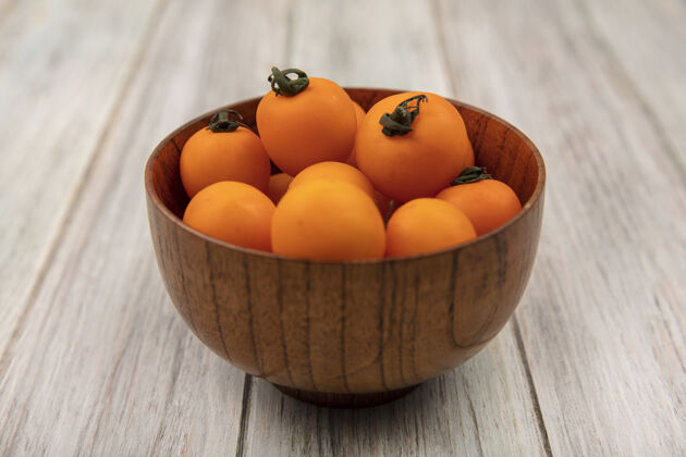 顶部橙色樱桃西红柿在灰色木质背景上的木碗顶视图樱桃景观碗