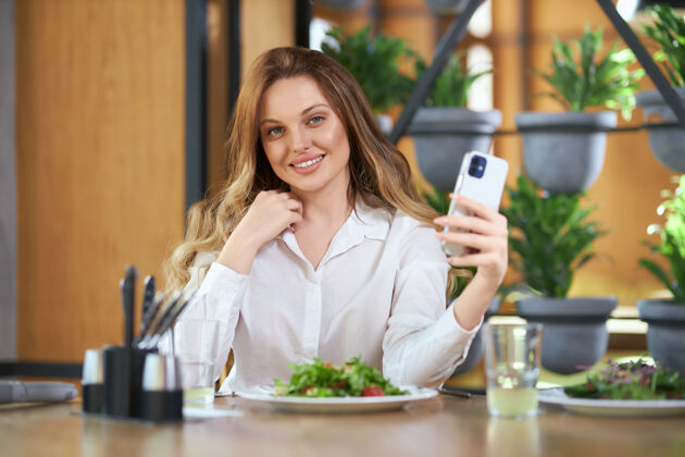 博客微笑的女人在现代手机上自拍制作午餐坐着