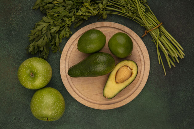 顶部木制菜板上梨形鳄梨的俯视图 绿色背景上隔离着青苹果和欧芹的酸橙食品景观形状