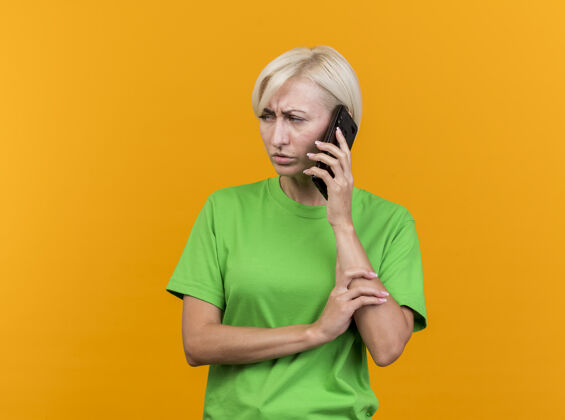 手臂皱眉的中年金发斯拉夫女人在讲电话 手挽着手看着隔离在黄色墙壁上的一面 还有复印空间站着人人