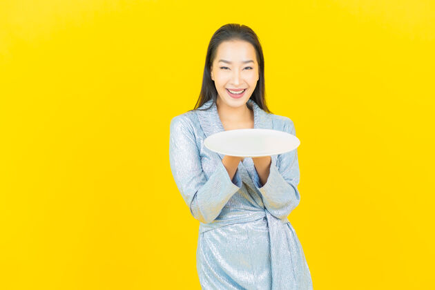 年轻人画像美丽的亚洲年轻女子微笑着在黄色的墙上空盘子盘子饮食女人