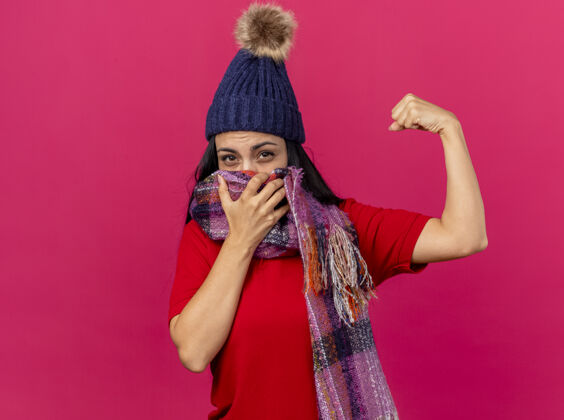 女孩自信的年轻生病的女人戴着冬天的帽子和围巾捂着嘴用围巾看着前面做着强烈的手势隔离在粉红色的墙壁上复制空间脸围巾姿势
