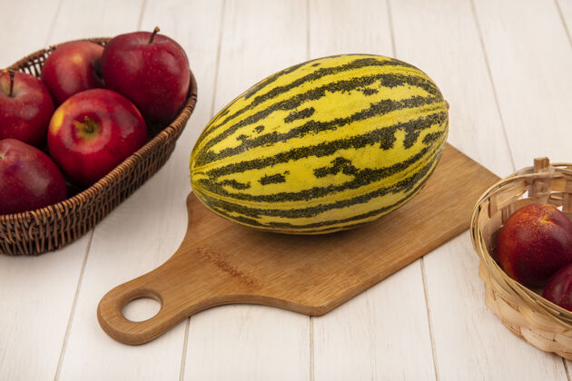 饮食有机哈密瓜的俯视图在木制的厨房板上 苹果放在桶上 桃子放在白色的木制背景上板瓜水果