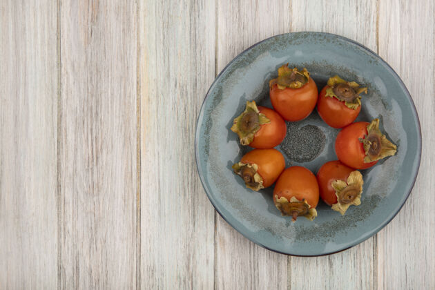 顶部在灰色木质背景上的盘子上 可以看到熟透的新鲜柿子的顶视图 还有复制空间盘子水果空间