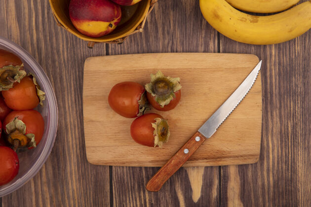 刀木制菜板上的多汁柿子俯视图 木桶上放着桃子和香蕉 木桶的背景是孤立的桃子柿子新鲜