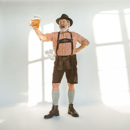 文化啤酒节高级男士的肖像 戴着帽子 穿着传统的巴伐利亚服装在白色背景的摄影棚拍摄的男性全长庆祝 节日 节日的概念喝啤酒表达德语啤酒
