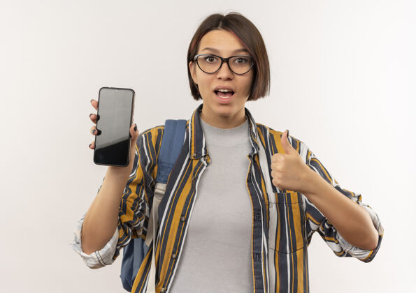 学生印象深刻的年轻女学生戴着眼镜 背着书包 展示着手机和大拇指 孤立地站在白色上展示包眼镜