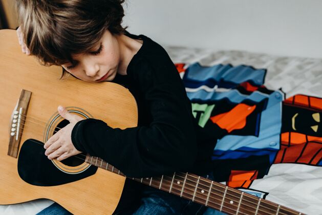 声学年轻的金发男孩坐在床上拿着吉他吉他手艺术家播放器