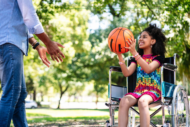 女孩一个坐在轮椅上的小女孩和她的父亲一起在公园玩篮球爱好一起享受